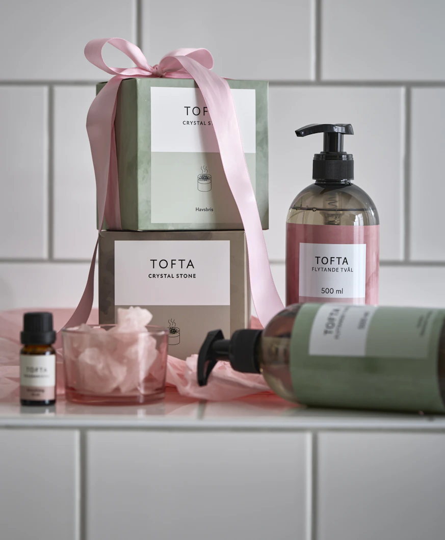 Paket med doftstenar omslagna med en rosa rosett och handtvål står framför en kaklad vägg.