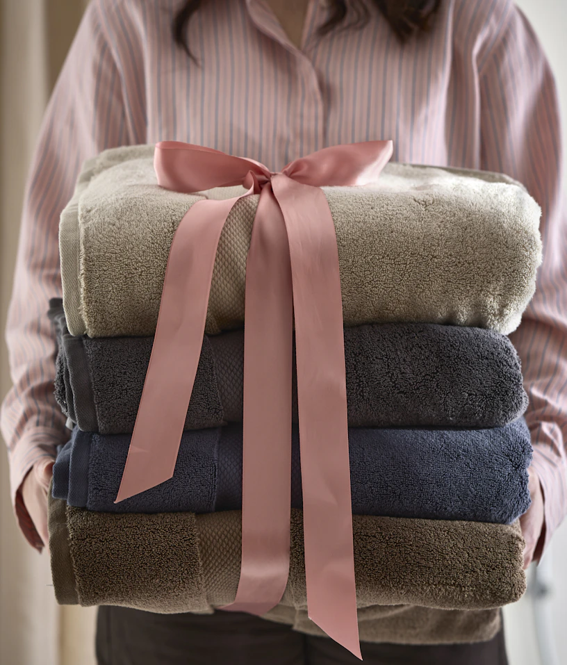 En kvinna håller i flera handdukar som har en rosa rosett om sig.