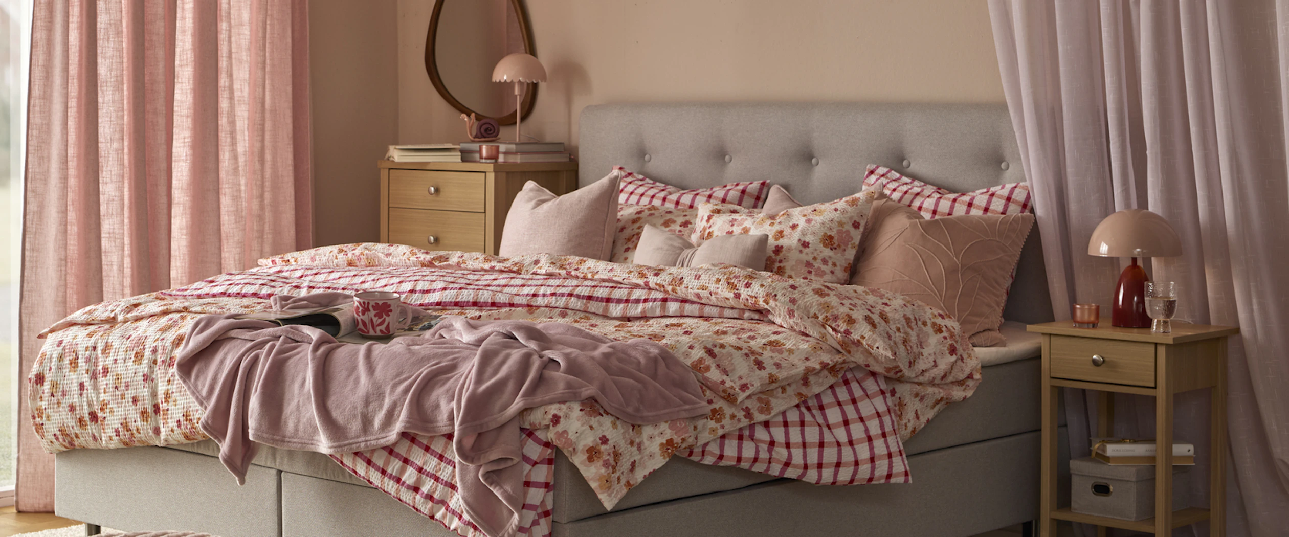 en grå säng bäddad med rosa påslakan i olika mönster står i ett sovrum