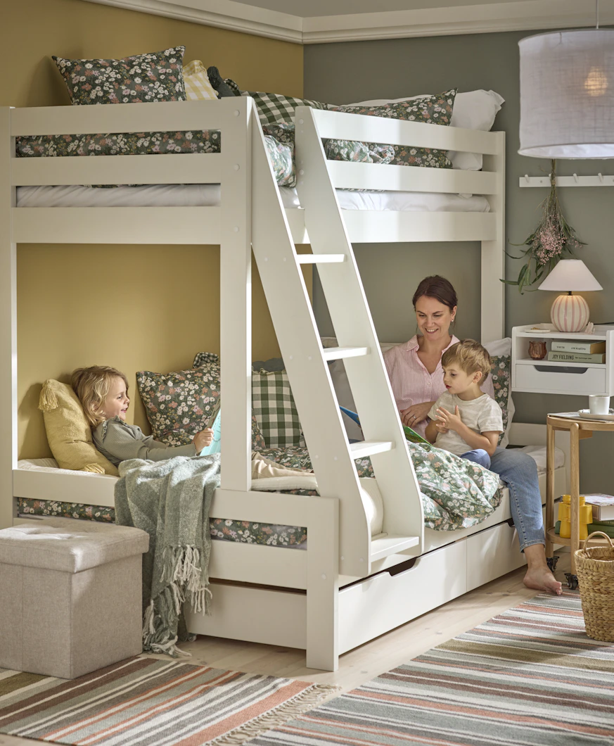 En kvinna och två barn läser bok i en våningssäng bäddad med grönblommiga sängkkäder.