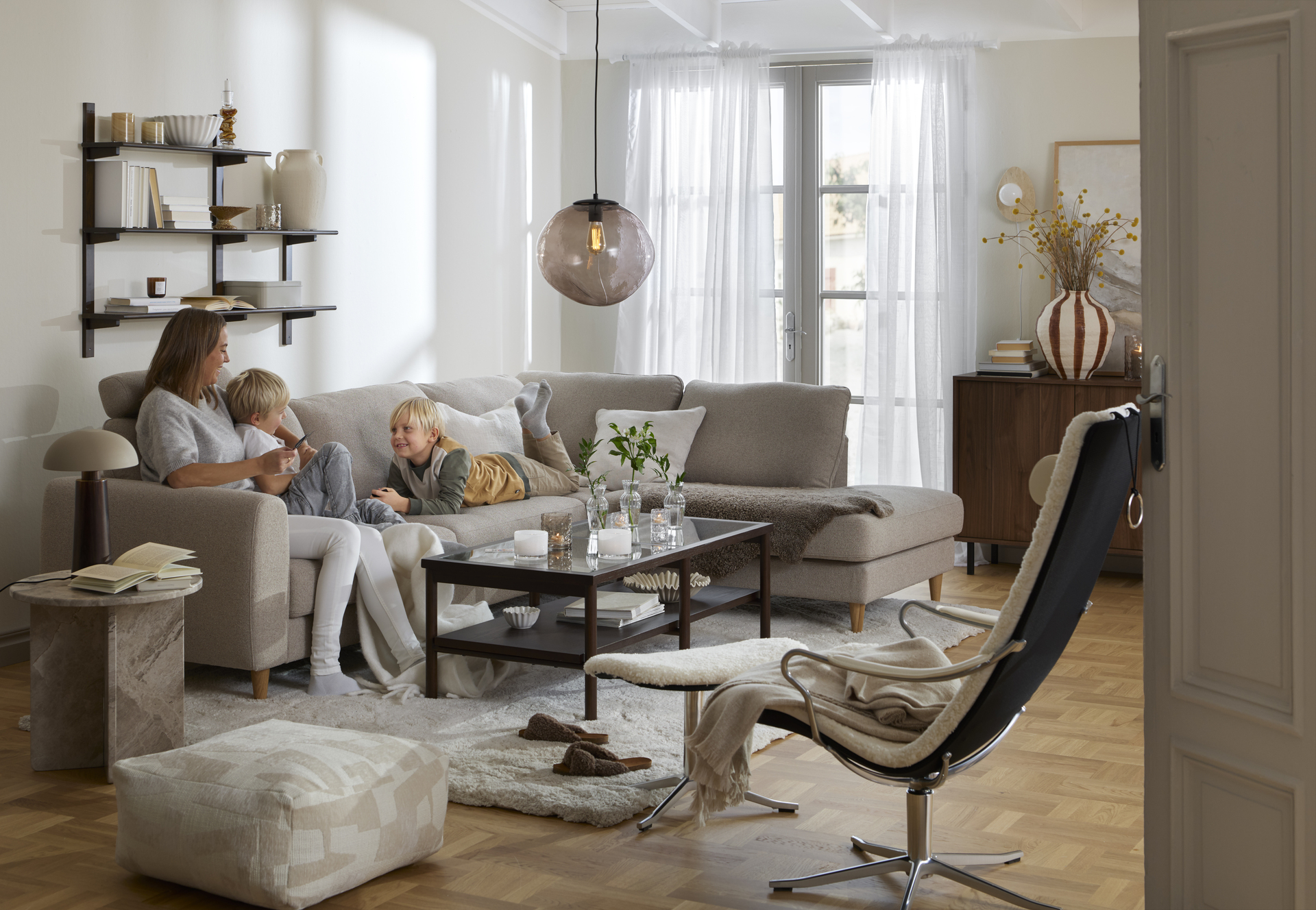 I en beige divansoffa sitter en kvinna och två barn