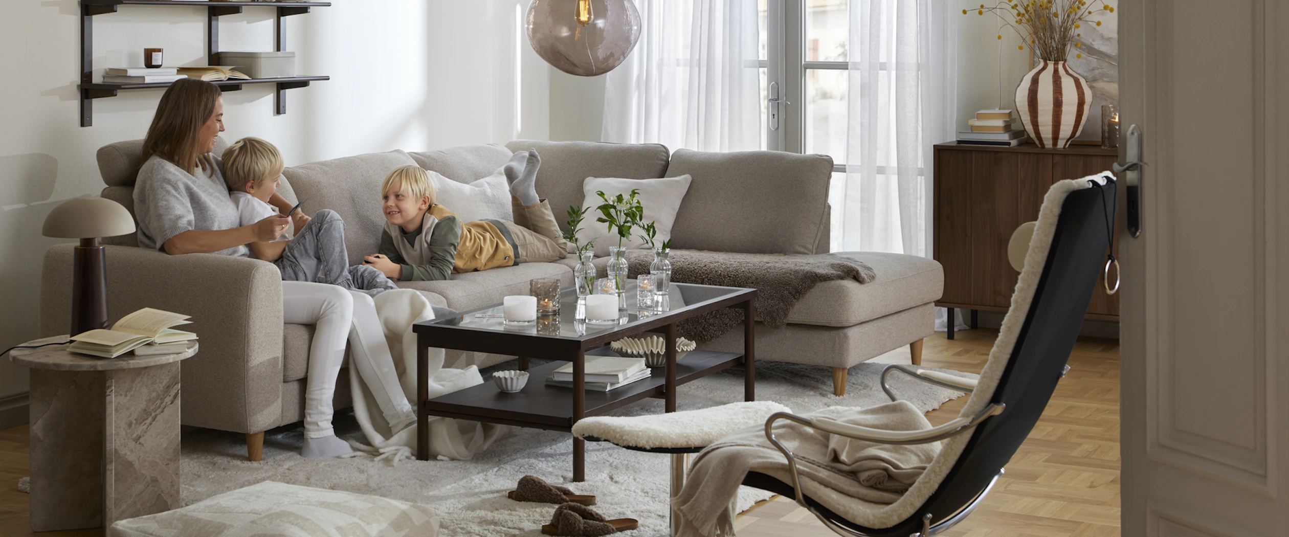 I en beige divansoffa sitter en kvinna och två barn