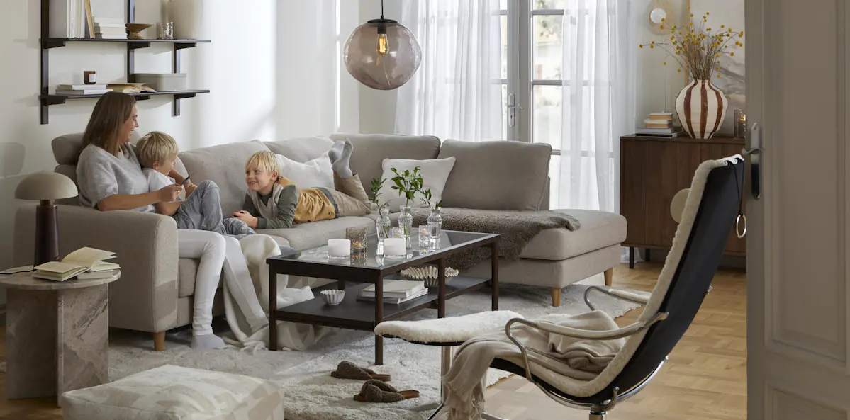 I en beige divansoffa sitter en kvinna och två barn