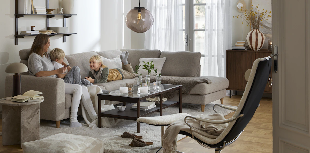 I en beige divansoffa sitter en kvinna och två barn