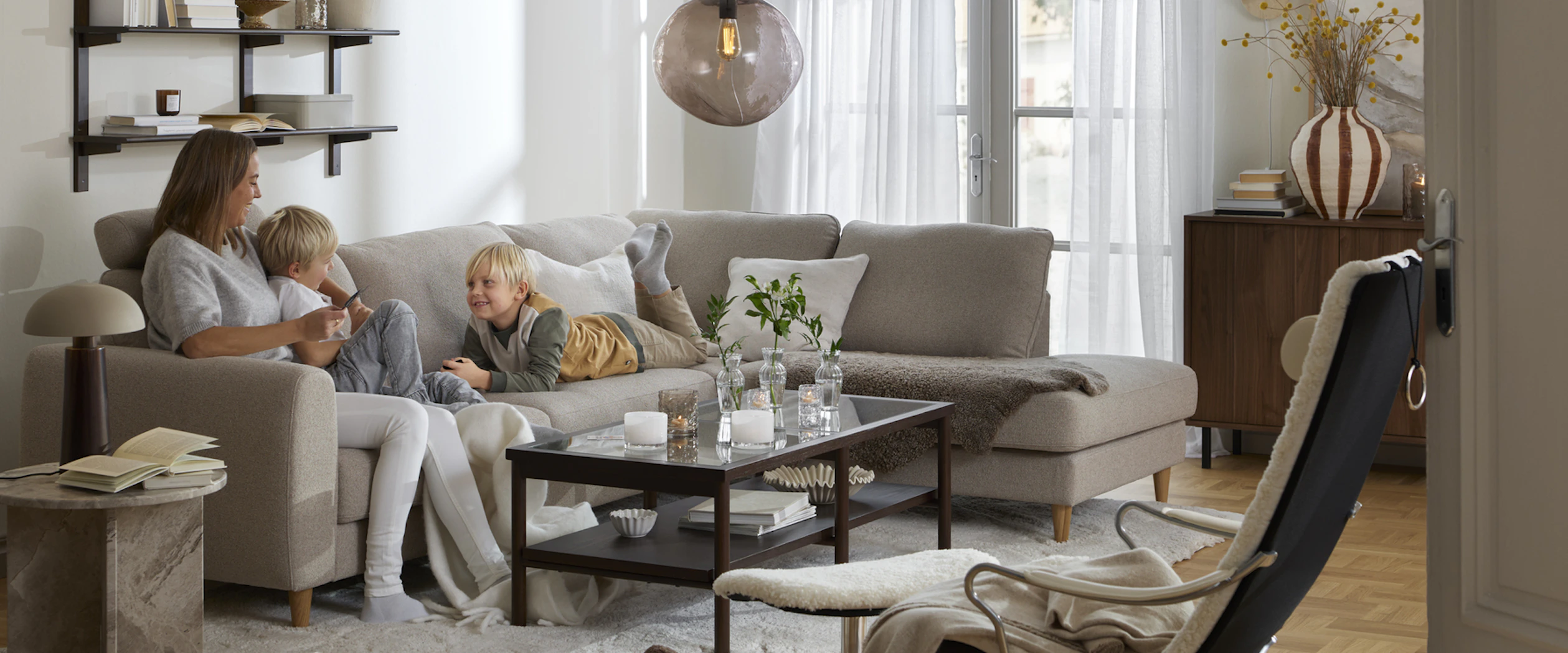 I en beige divansoffa sitter en kvinna och två barn
