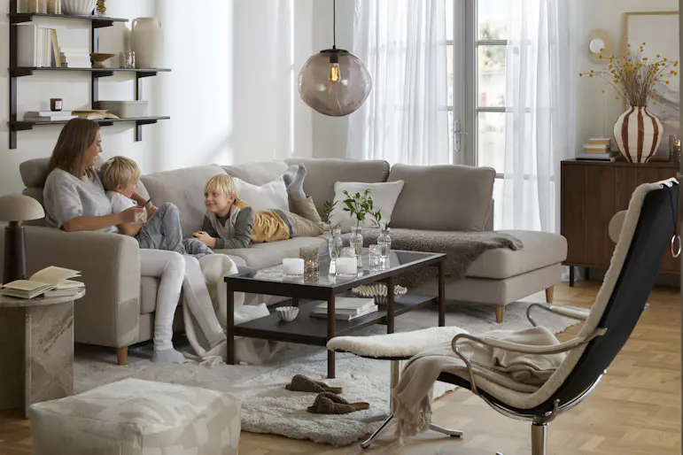 I en beige divansoffa sitter en kvinna och två barn