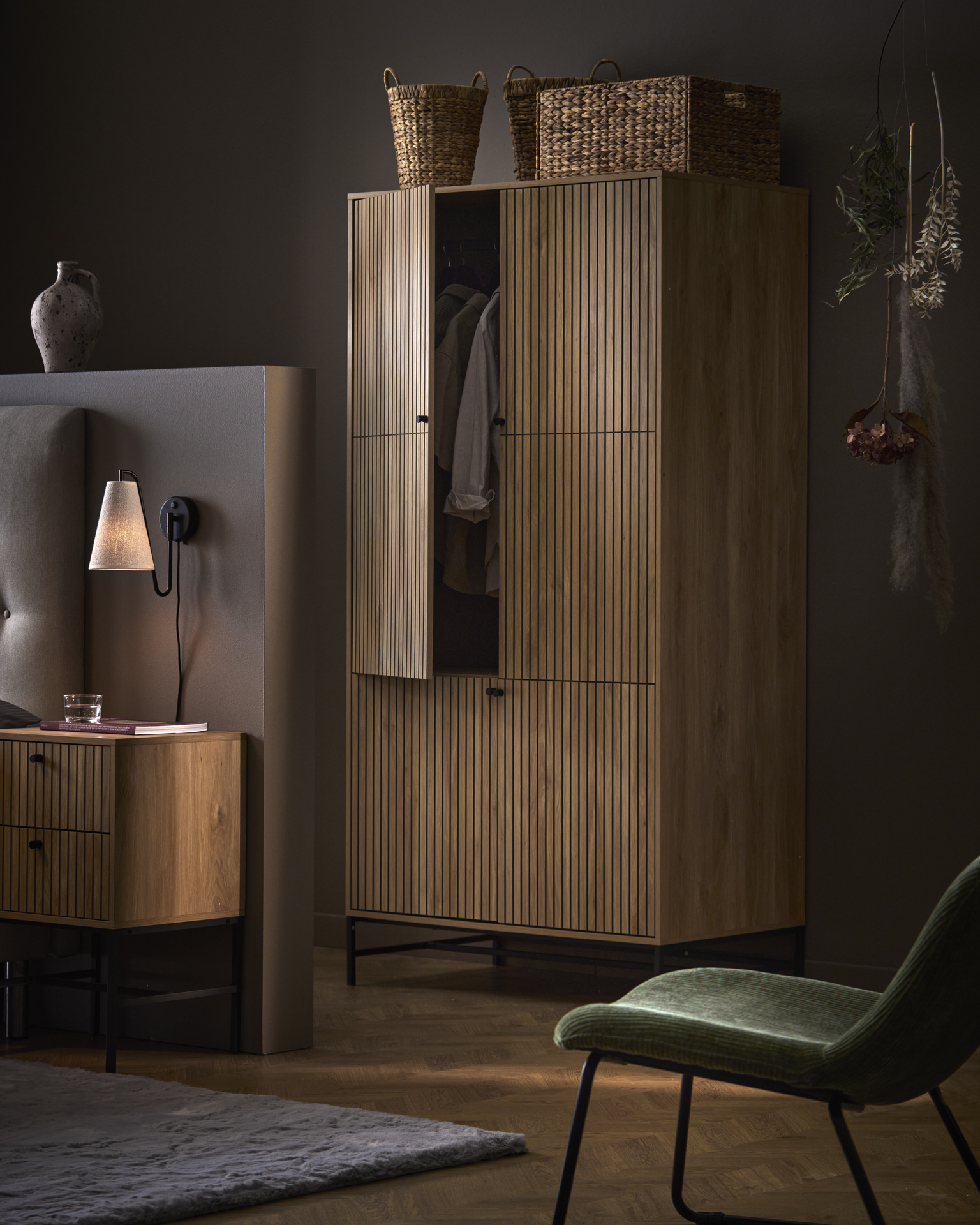 En garderob i mörkt trä med ribbor och matchande sängbord står i ett mörkt sovrum.