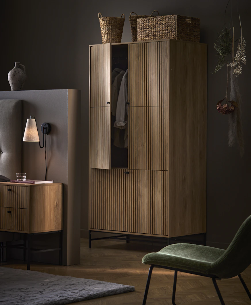 En garderob i mörkt trä med ribbor och matchande sängbord står i ett mörkt sovrum.