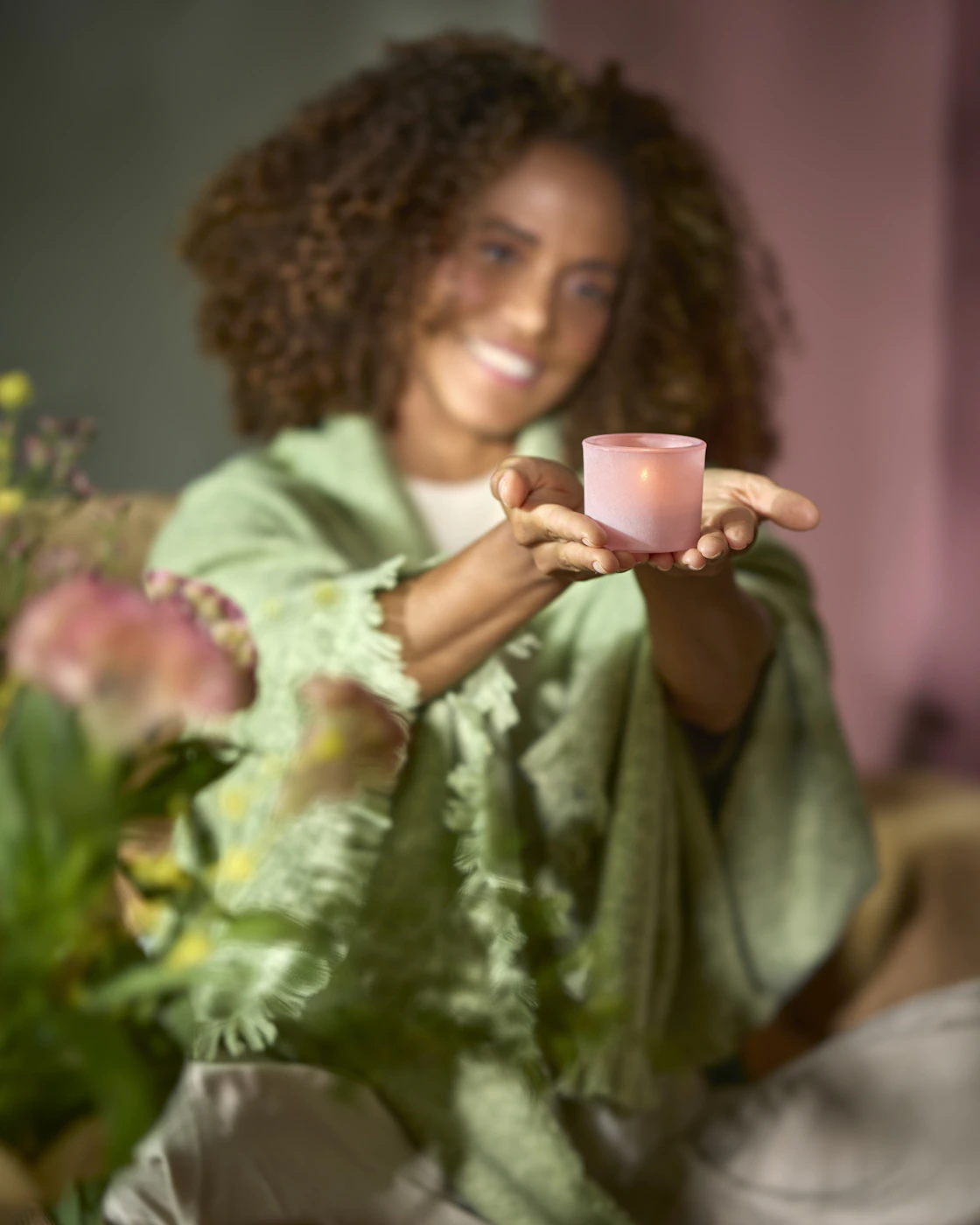 En kvinna invirad i en grön pläd håller upp en rosa ljuslykta.
