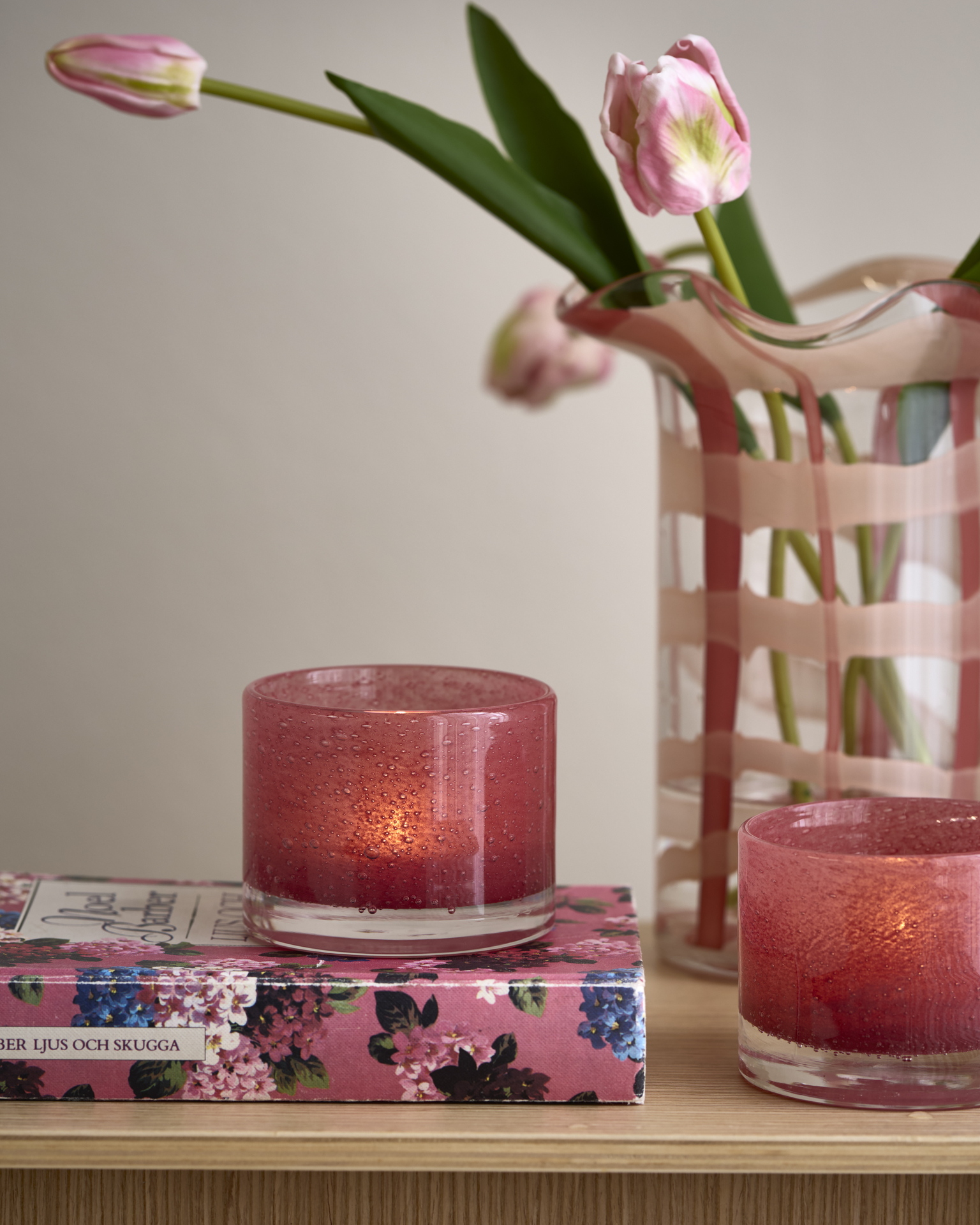 en rosa ljuslykta står på en rosa bok bredvid en vas