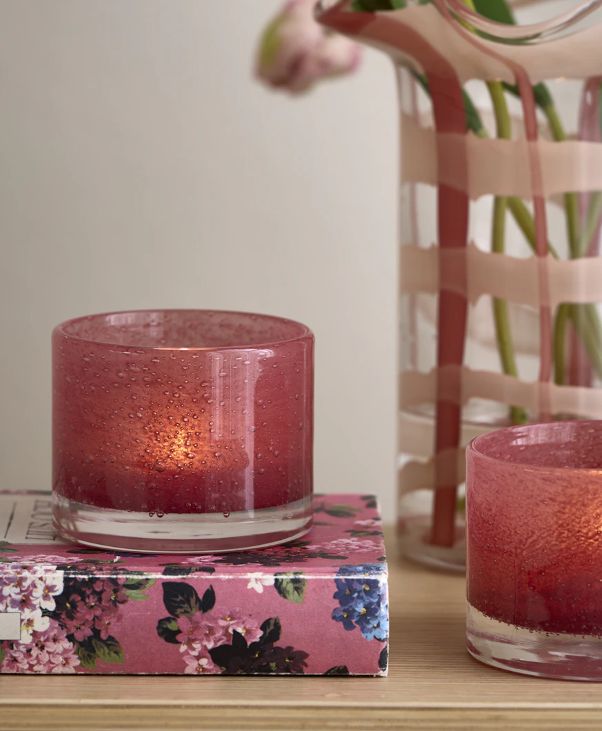 en rosa ljuslykta står på en rosa bok bredvid en vas