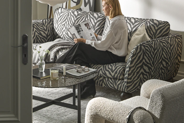 I ett stilrent vardagsrum sitter en kvinna i en zebramönstrad soffa