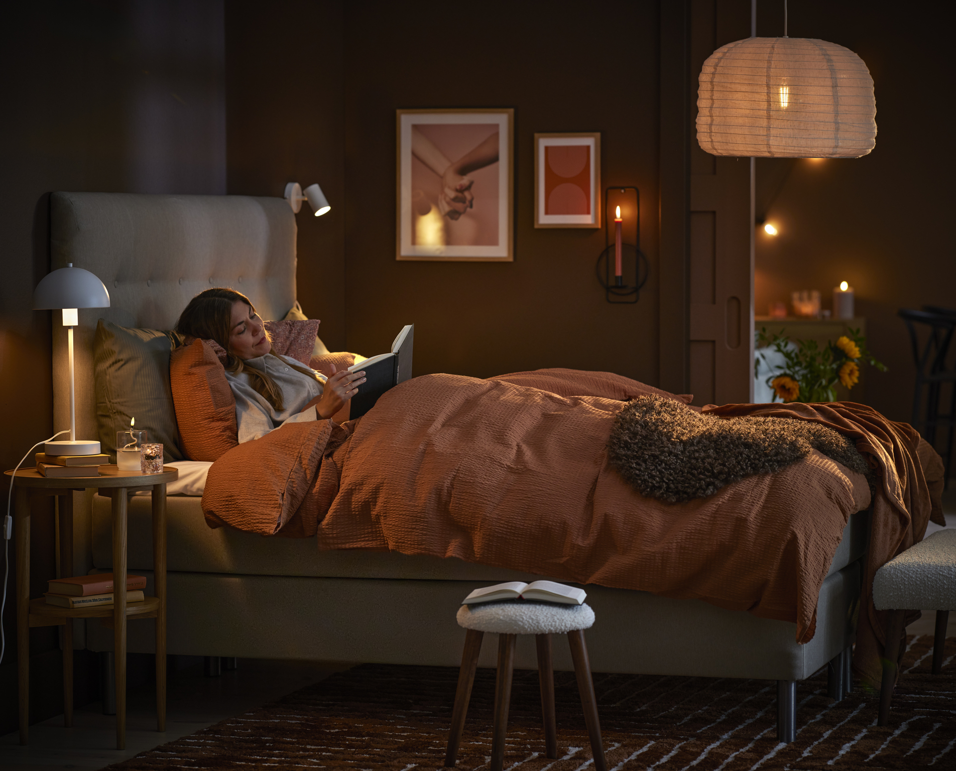 Ung kvinna ligger i mörkt sovrum och läser en bok i sängen. 