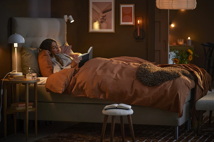 Ung kvinna ligger i mörkt sovrum och läser en bok i sängen.