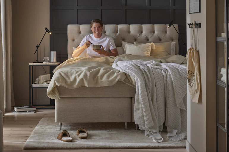 Skidåkaren William Poromaa sitter i en kontinentalsäng från Mio och äter en skål med gröt.