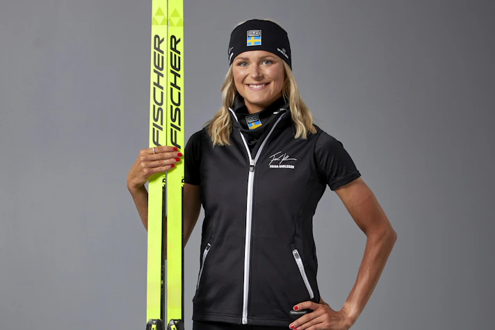 Porträttbild på skidåkaren Frida Karlsson i träningskläder med stavar och skidor.