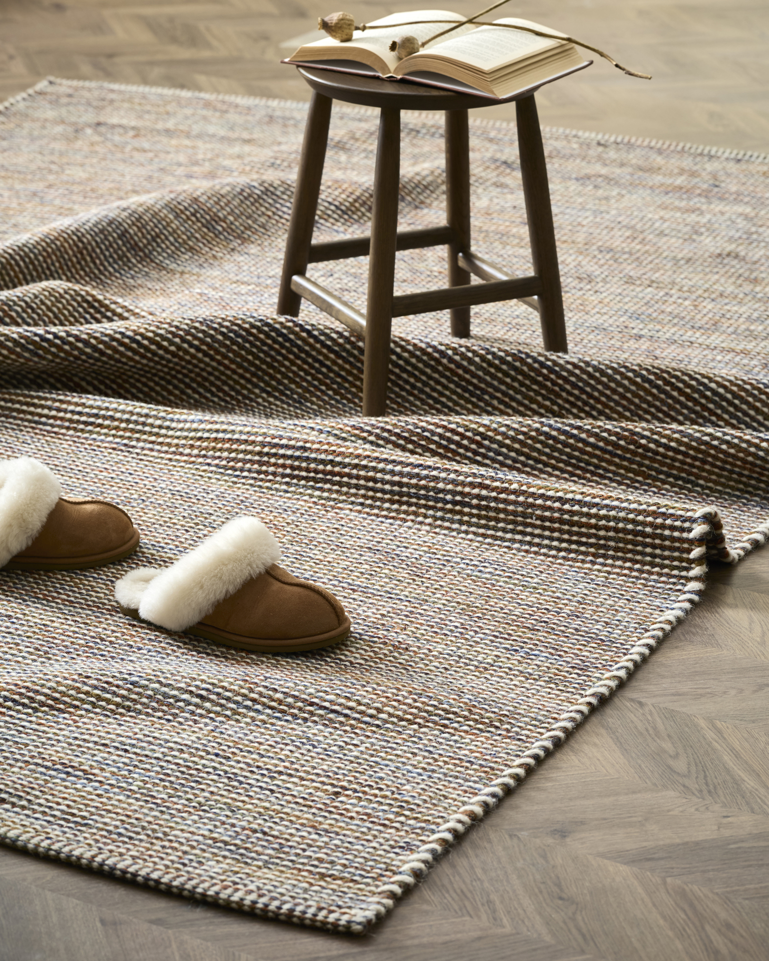 en brun ullmatta ligger på ett trägolv, samt ett par tofflor och en pall