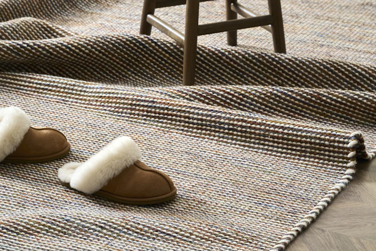 en brun ullmatta ligger på ett trägolv, samt ett par tofflor och en pall