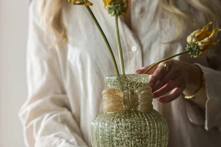 en person med vit skjorta håller en grön vas framför sig