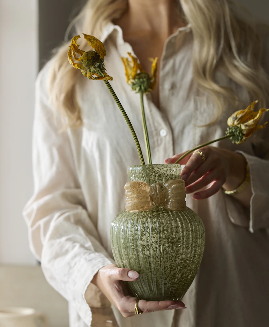 en person med vit skjorta håller en grön vas framför sig