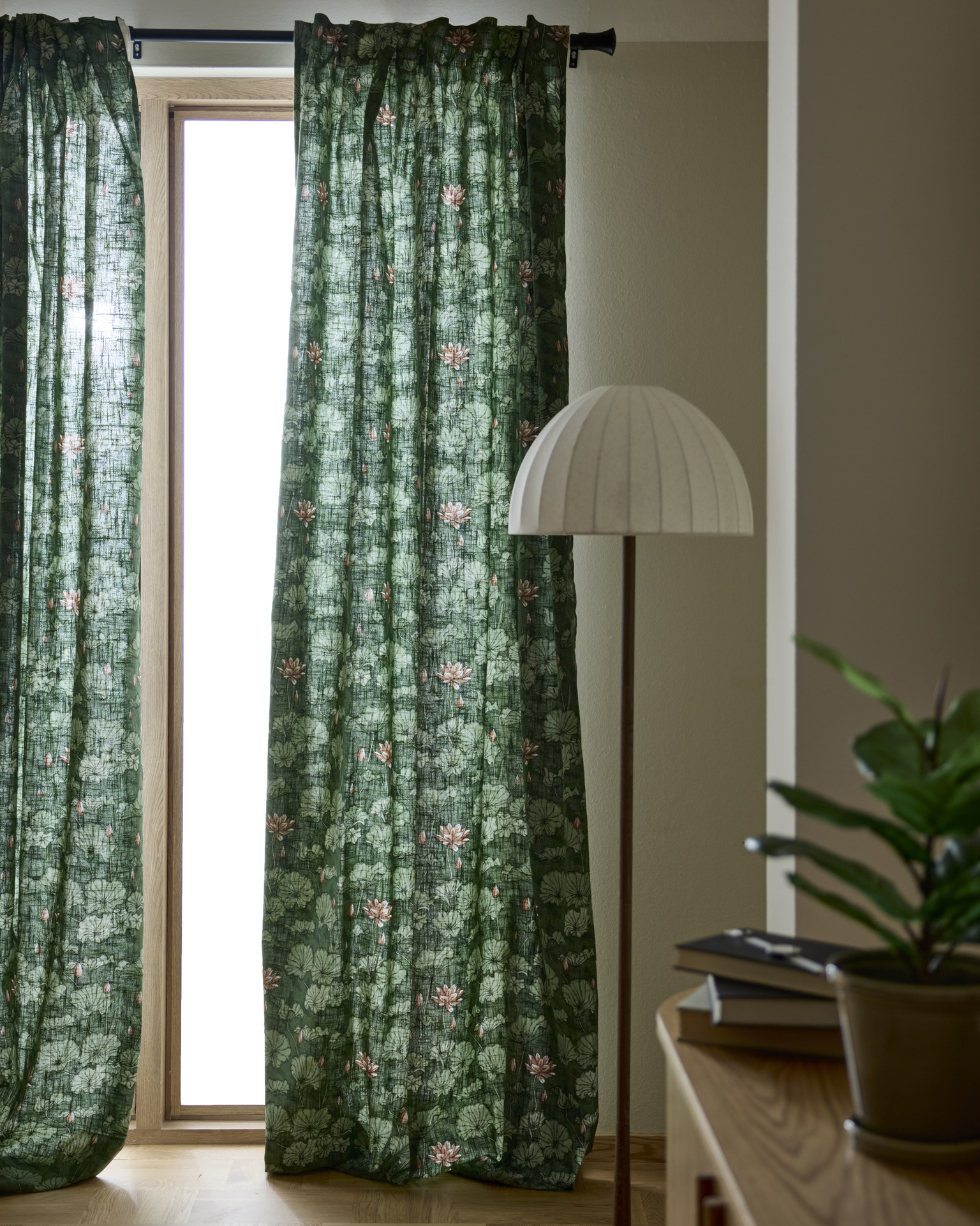 gröna gardiner med blommönster hänger framför ett stort fönster bredvid en stor golvlampa
