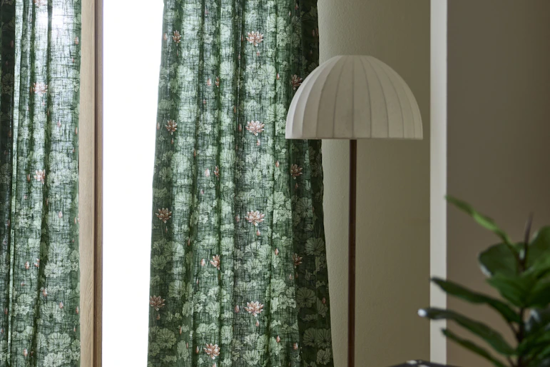 gröna gardiner med blommönster hänger framför ett stort fönster bredvid en stor golvlampa