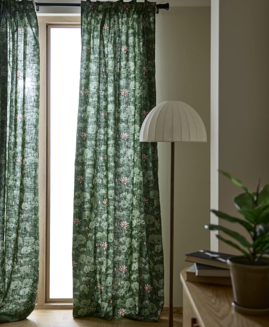 gröna gardiner med blommönster hänger framför ett stort fönster bredvid en stor golvlampa