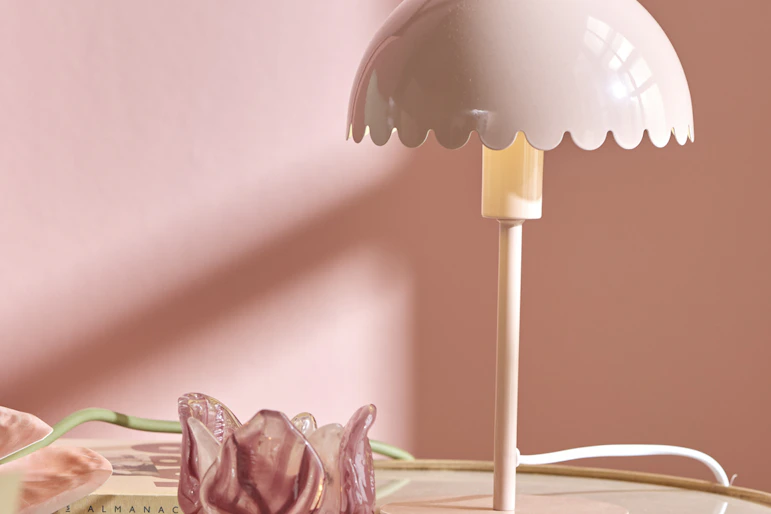 en rosa bordslampa står på ett runt sidobord framför en rosa vägg