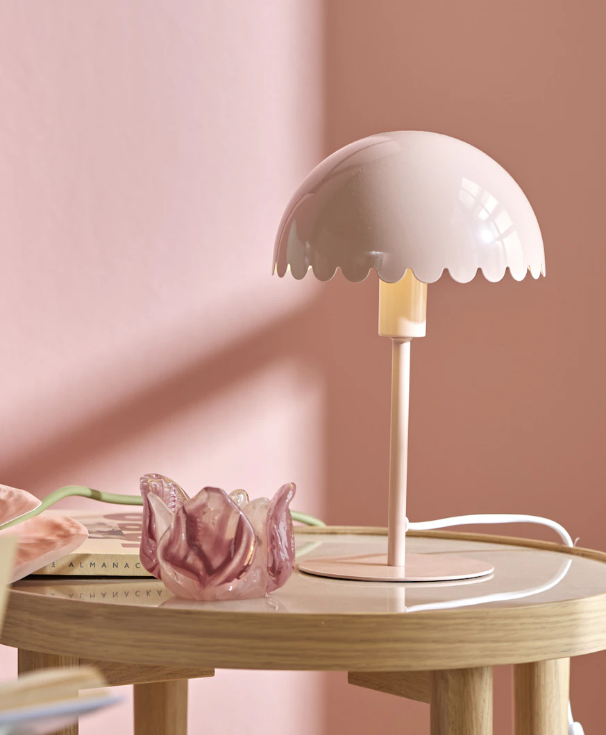 en rosa bordslampa står på ett runt sidobord framför en rosa vägg