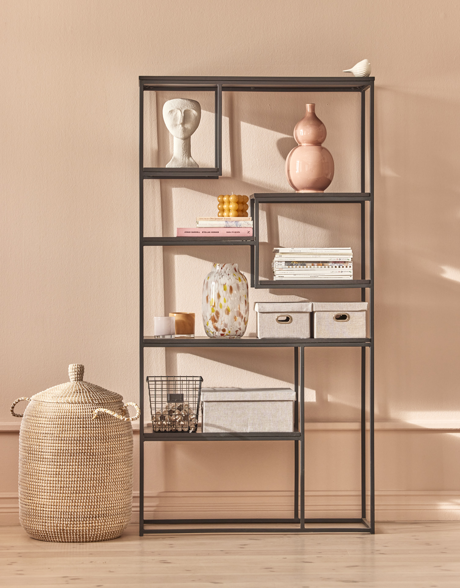 en svart hylla står framför en rosa vägg med olika dekorationer 