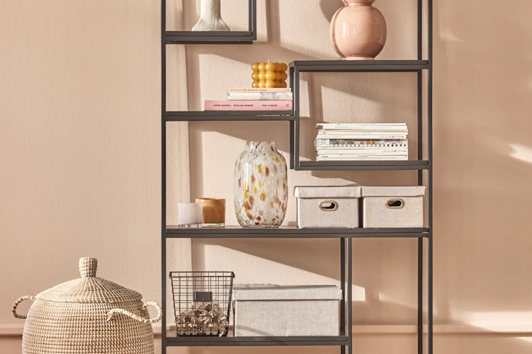 en svart hylla står framför en rosa vägg med olika dekorationer