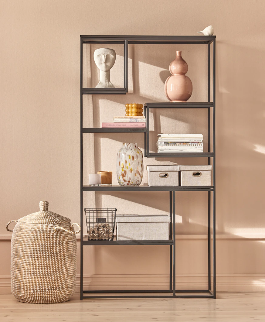 en svart hylla står framför en rosa vägg med olika dekorationer