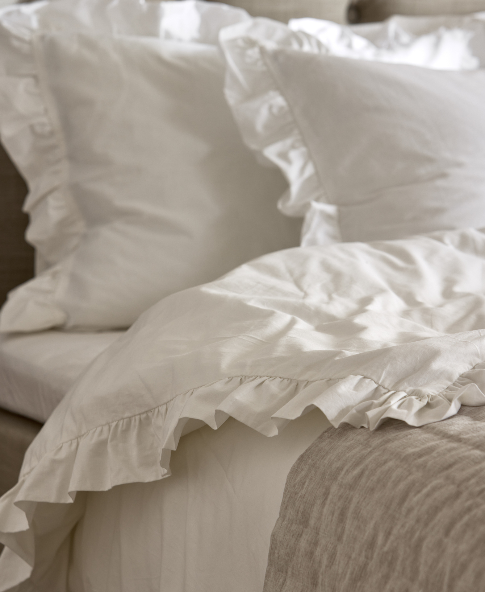 en säng bäddad med vita påslakan och örngott med volanger