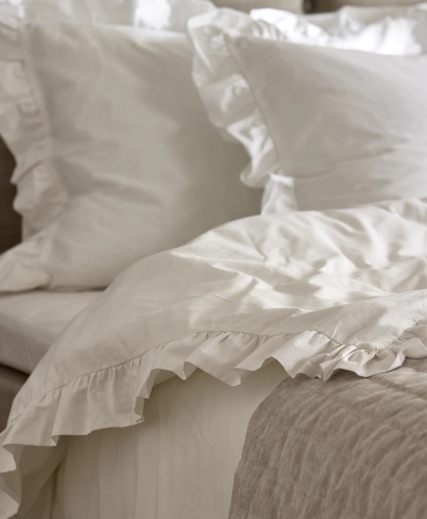 en säng bäddad med vita påslakan och örngott med volanger