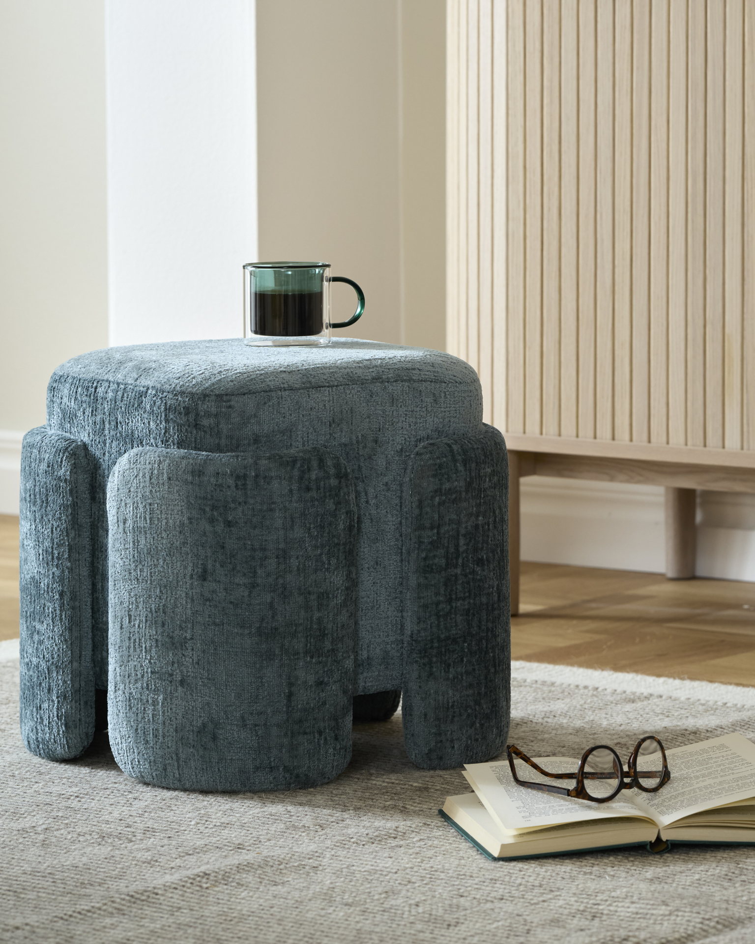 en grön kaffekopp står på en blå puff som är placerad på en beige matta 