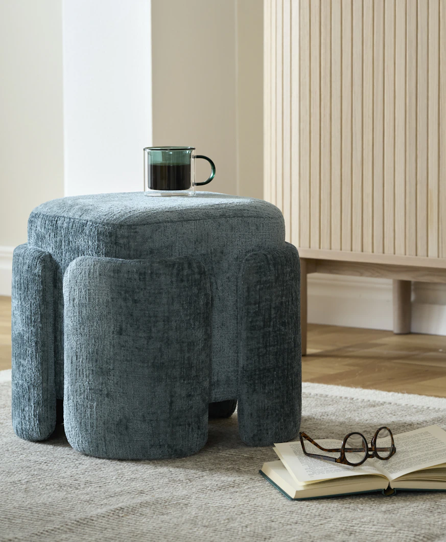 en grön kaffekopp står på en blå puff som är placerad på en beige matta