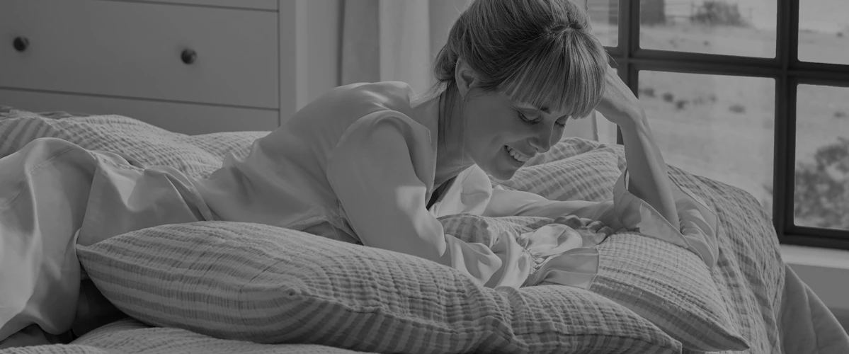 Kvinna som ligger på mage i säng och ser ut att skratta åt något, bild i gråskala.