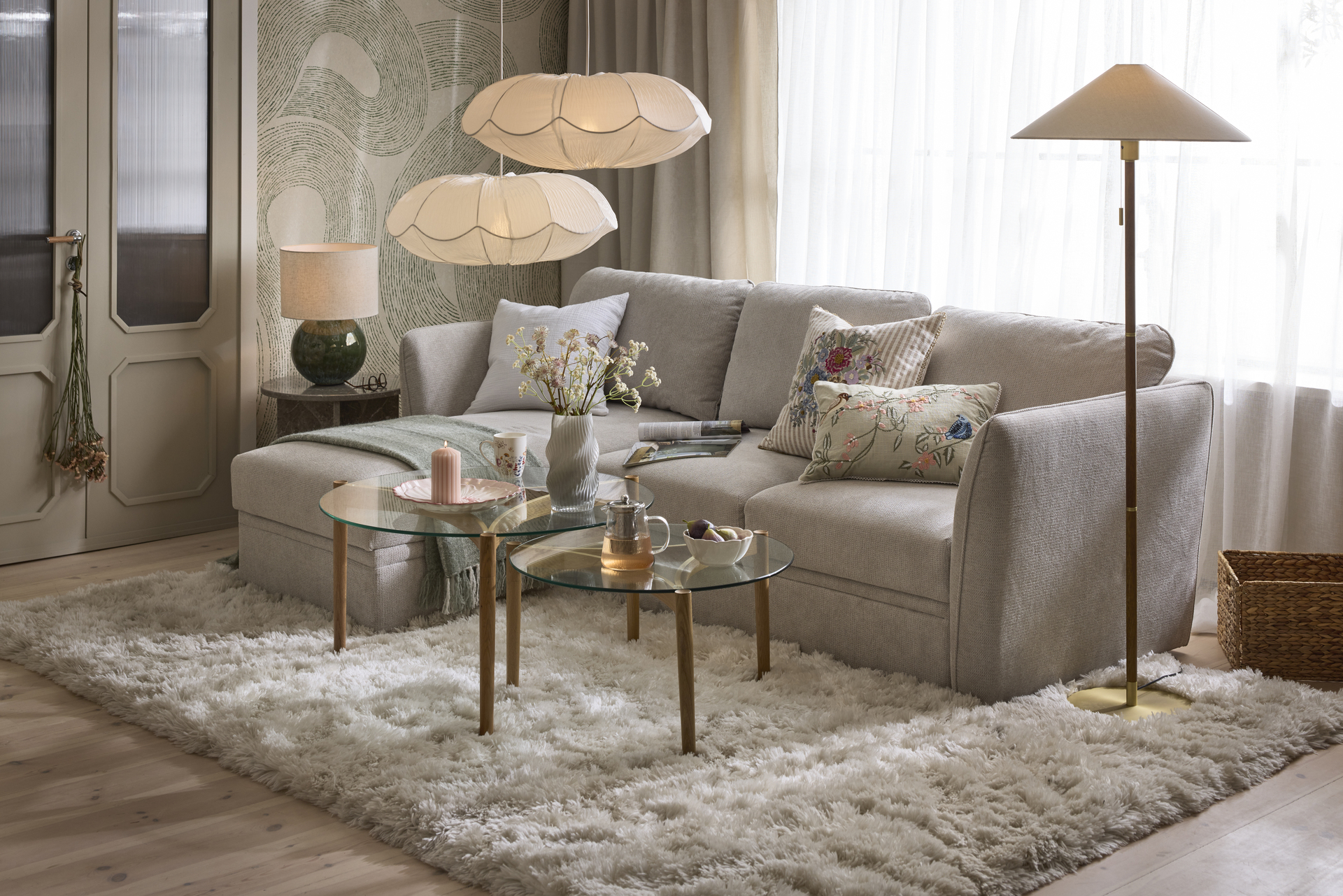 en grå bäddsoffa står i ett vardagsrum med en stor vit matta och soffbord i glas