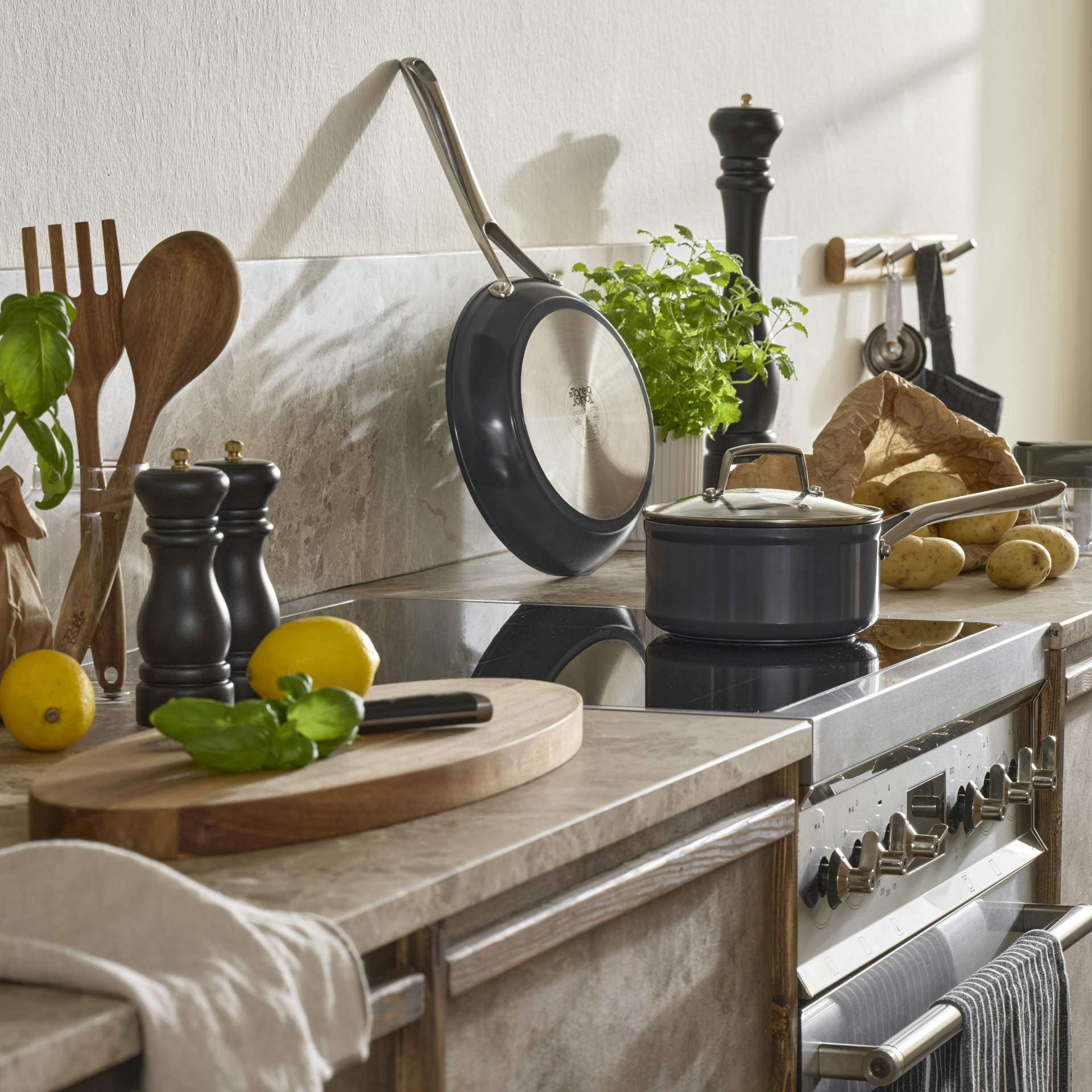 På en spis står en kastrull och på köksbänken bredvid står en mängd olika köksredskap