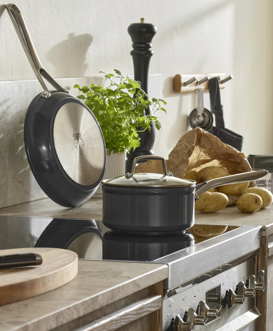 På en spis står en kastrull och på köksbänken bredvid står en mängd olika köksredskap