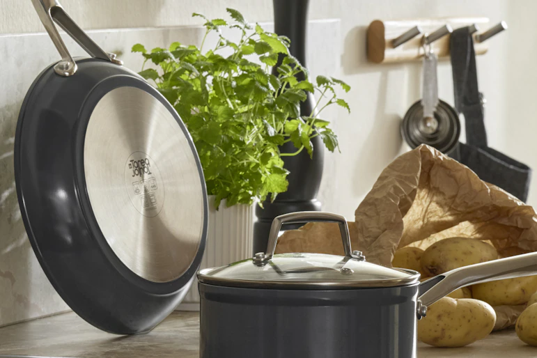 På en spis står en kastrull och på köksbänken bredvid står en mängd olika köksredskap