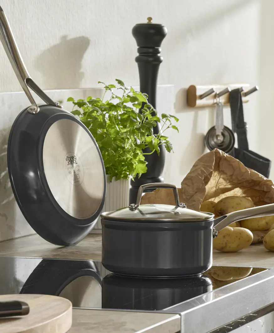 På en spis står en kastrull och på köksbänken bredvid står en mängd olika köksredskap