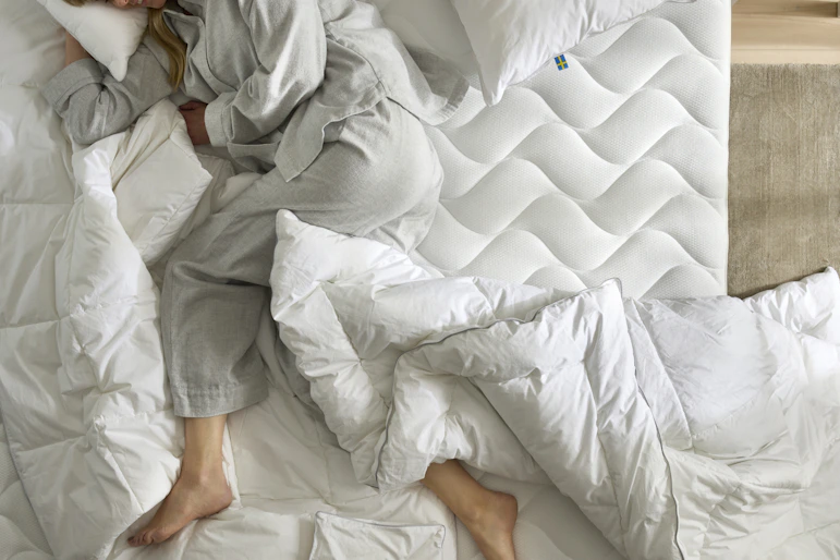 en tjej ligger på en obäddad bäddmadrass med ett täcke och kudde