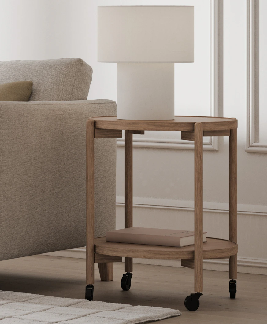 en vit lampa står på ett ljust sidobord i trä bredvid en soffa