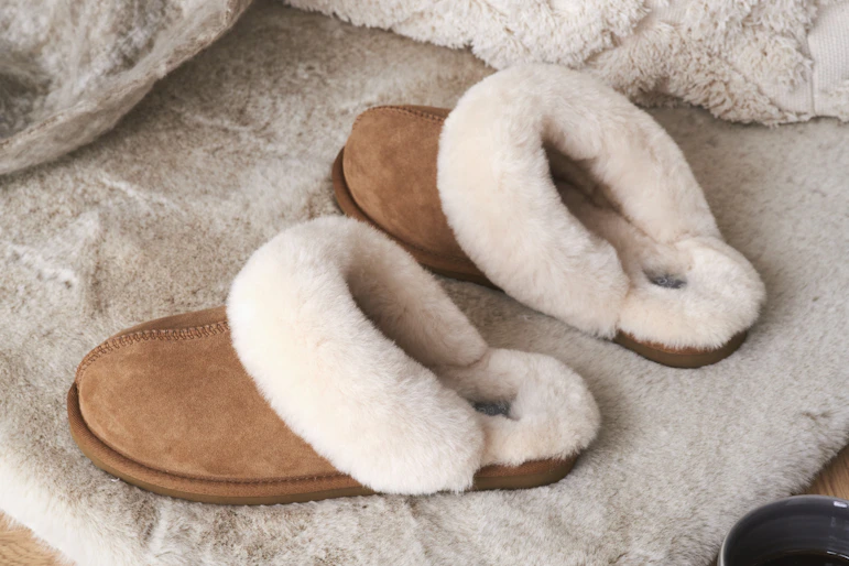 bruna fårskinnstofflor står på en beige matta