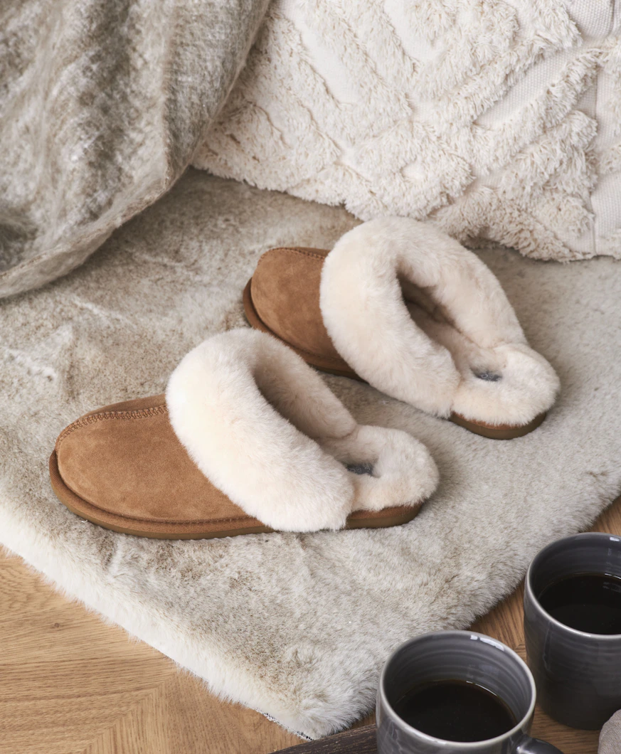 bruna fårskinnstofflor står på en beige matta