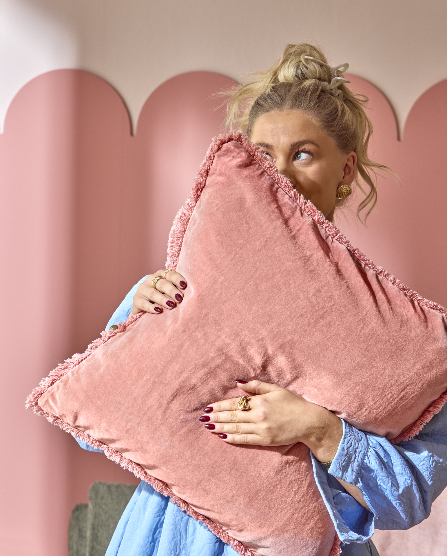 en blond tjej står och håller upp en rosa kudde framför ansiktet