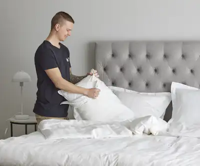 Ung man står intill en dubbelsäng och byter örngott på en kudde