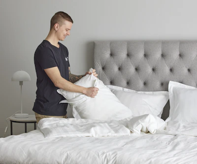 Ung man står intill en dubbelsäng och byter örngott på en kudde