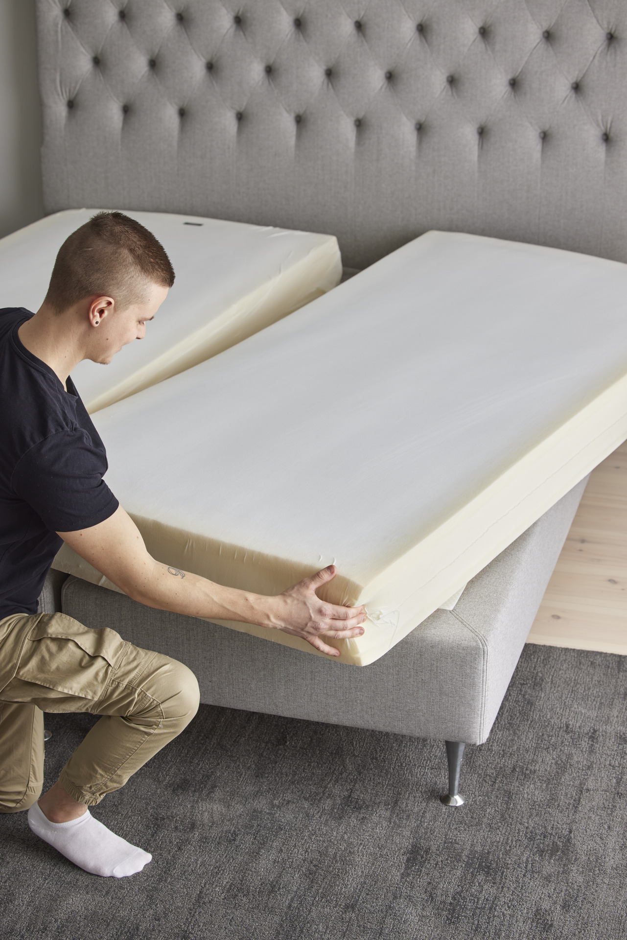 Ung man står på ena knät intill en säng och vrider på sängkassetten. 